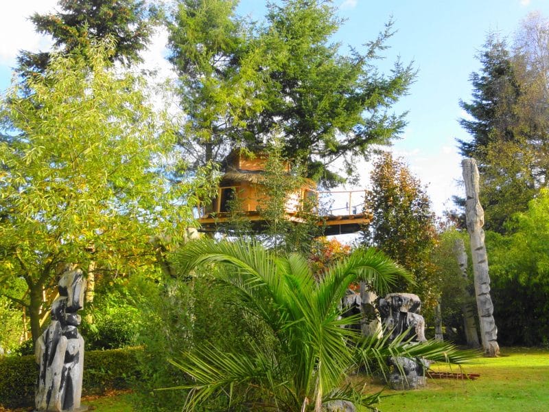 Cabane dans les arbres entourée de sculptures et de verdure luxuriante.