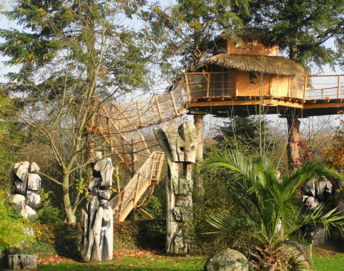 Cabane dans les arbres en Bretagne, entourée de sculptures en bois et verdure luxuriante.