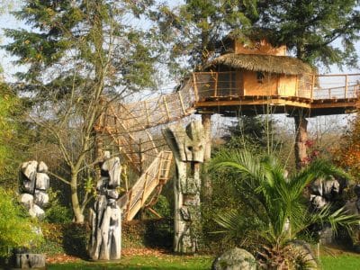Cabane dans les arbres en Bretagne, entourée de sculptures en bois et verdure luxuriante.
