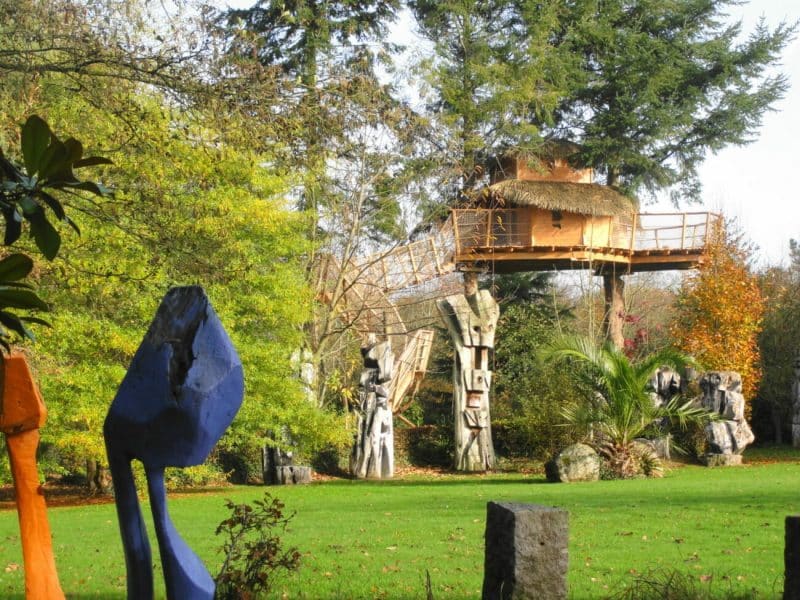 Cabane dans les arbres entourée de sculptures colorées et dune verdure luxuriante.