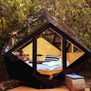 Cabane en verre moderne, nichée dans la nature, avec un lit confortable et des vues dégagées.
