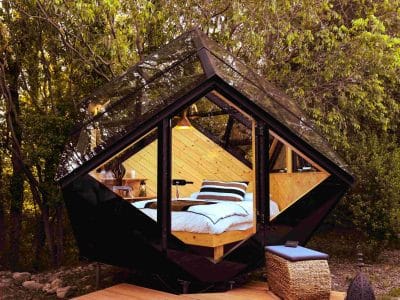 Cabane en verre moderne, nichée dans la nature, avec un lit confortable et des vues dégagées.
