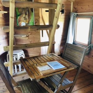 Cabane en bois avec échelle, table en bois et décoration chaleureuse.