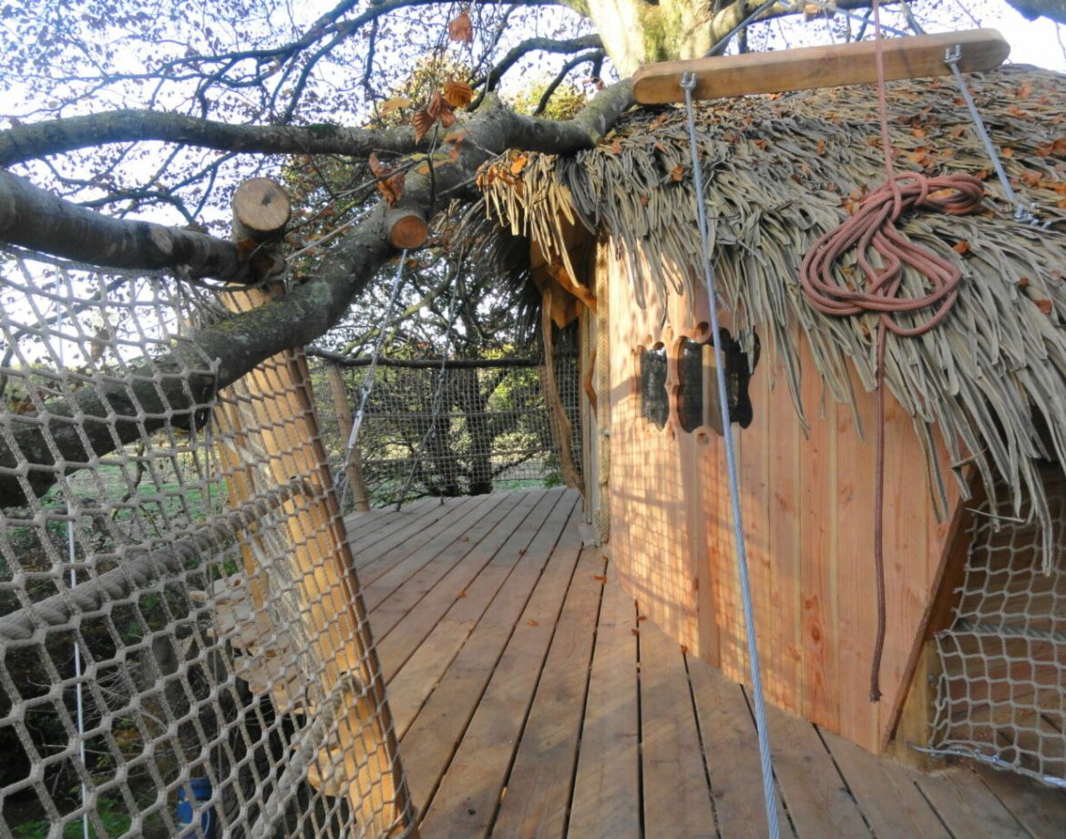 Cabane perchée en Bretagne, toit en chaume et terrasse en bois suspendue.