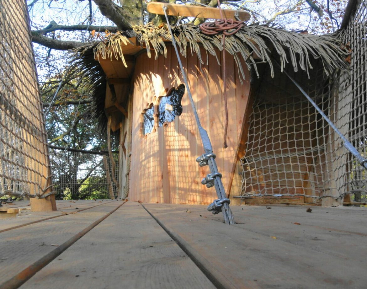 Cabane dans les arbres en Bretagne, avec un toit en chaume et des fenêtres découpées.