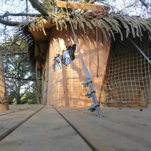Cabane dans les arbres en Bretagne, avec un toit en chaume et des fenêtres découpées.