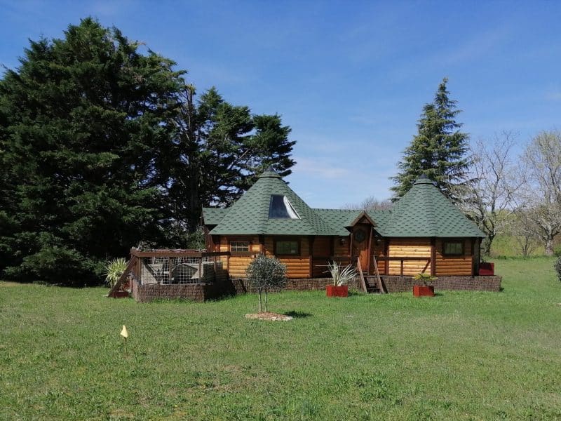 Charmante maison en bois avec toit en ardoise, entourée de verdure.