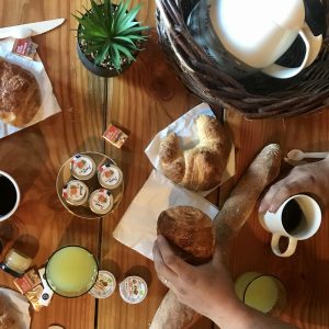 Petit-déjeuner convivial dans un gîte en bois, avec croissants et café sur table en bois.