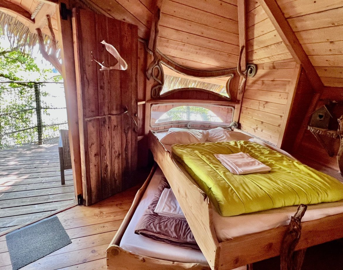 Cabane perchée en bois avec lit confortable et vue sur la nature environnante.