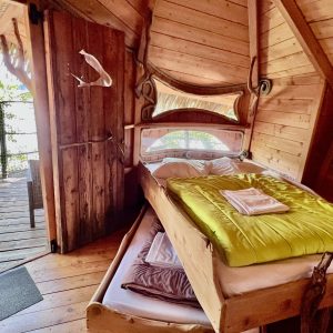 Cabane perchée en bois avec lit confortable et vue sur la nature environnante.