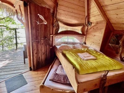 Cabane perchée en bois avec lit confortable et vue sur la nature environnante.