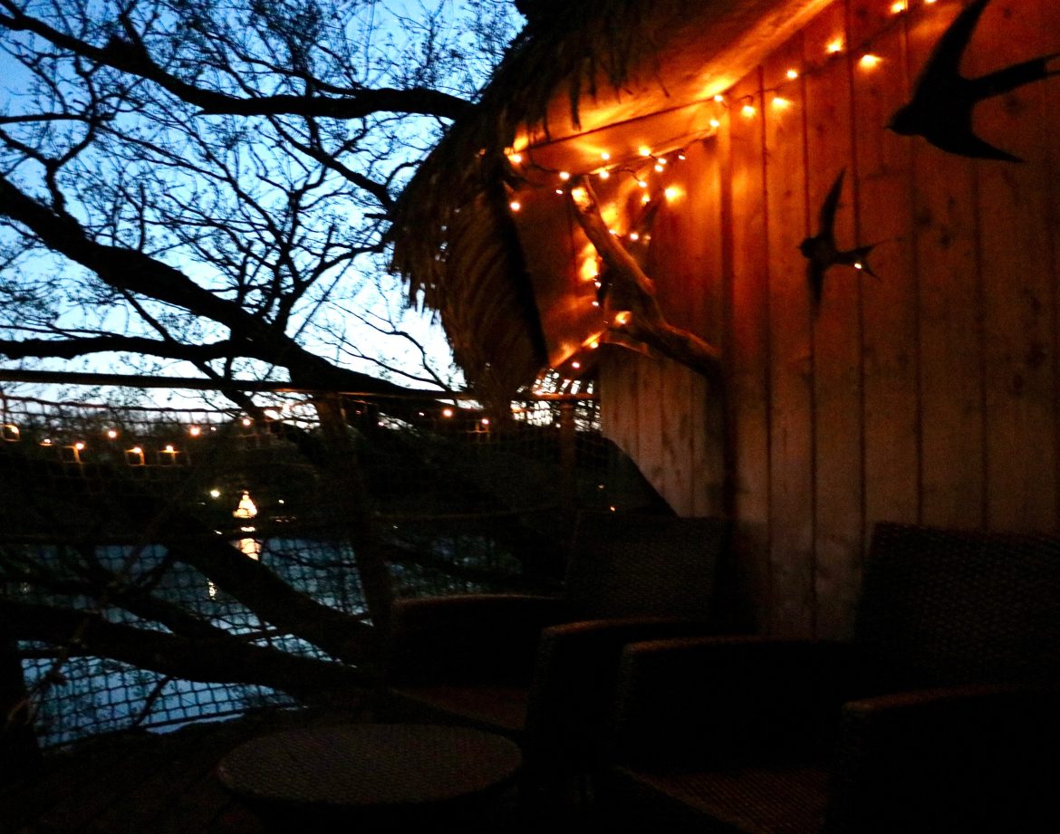 Cabane perchée en bois, illuminée par des guirlandes, au bord dun lac paisible.