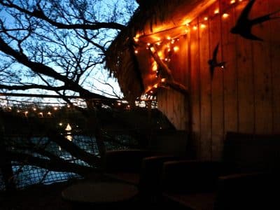 Cabane perchée en bois, illuminée par des guirlandes, au bord dun lac paisible.