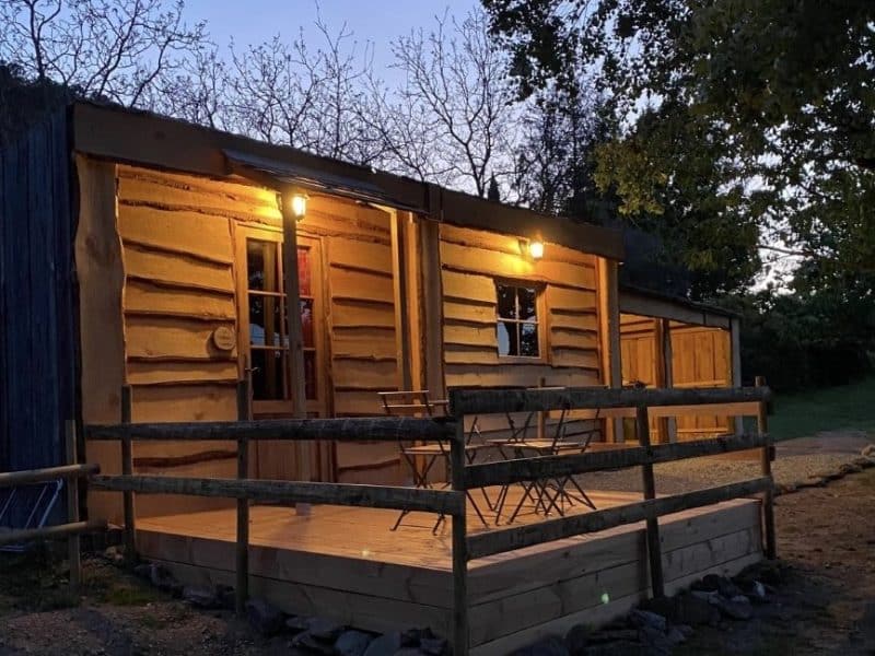 Cabane en bois avec terrasse, éclairée par des lanternes au crépuscule.