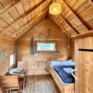 Cabane en bois chaleureuse avec lit douillet et table en bois, ambiance cosy.