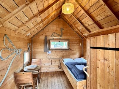 Cabane en bois chaleureuse avec lit douillet et table en bois, ambiance cosy.
