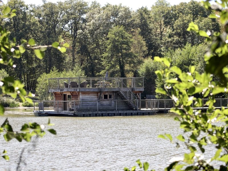 Cabane flottante en bois sur un lac, entourée de verdure luxuriante.