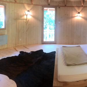 Cabane en bois avec lit douillet et décoration chaleureuse, située en pleine nature.