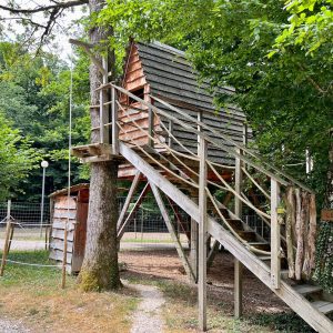 Cabane perchée en bois, entourée darbres, offrant une vue paisible sur la nature.