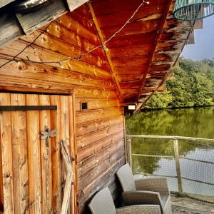 Cabane sur pilotis au bord de leau, avec une terrasse et des fauteuils confortables.