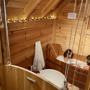 Cabane en bois avec baignoire en bois, ambiance chaleureuse et lumineuse.