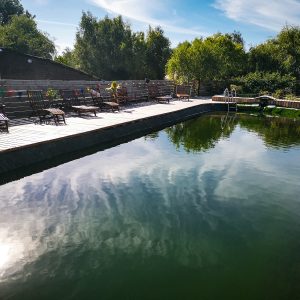 Hébergement insolite en Basse-Normandie avec piscine naturelle et chaises en bois.