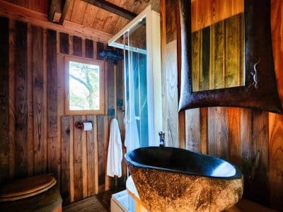 Cabane en bois à Limousin avec douche moderne et lavabo en pierre. Ambiance chaleureuse.