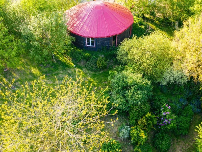 Yourte entourée de verdure, avec un toit rouge et un jardin fleuri.