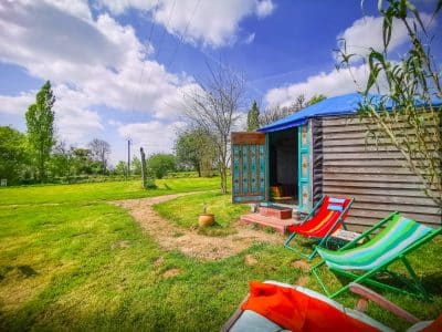 Cabane colorée en Basse-Normandie, entourée de verdure et chaises longues.