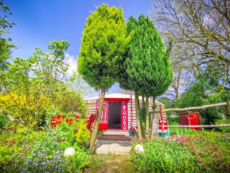 Cabane insolite en Basse-Normandie, entourée de verdure et de fleurs colorées.