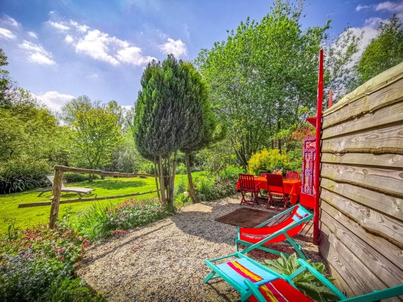 Chalet en pleine nature avec chaises colorées et jardin verdoyant.