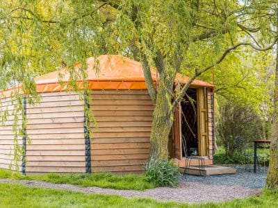 Yourte en bois avec toit orange, nichée sous des arbres verdoyants en Basse-Normandie.