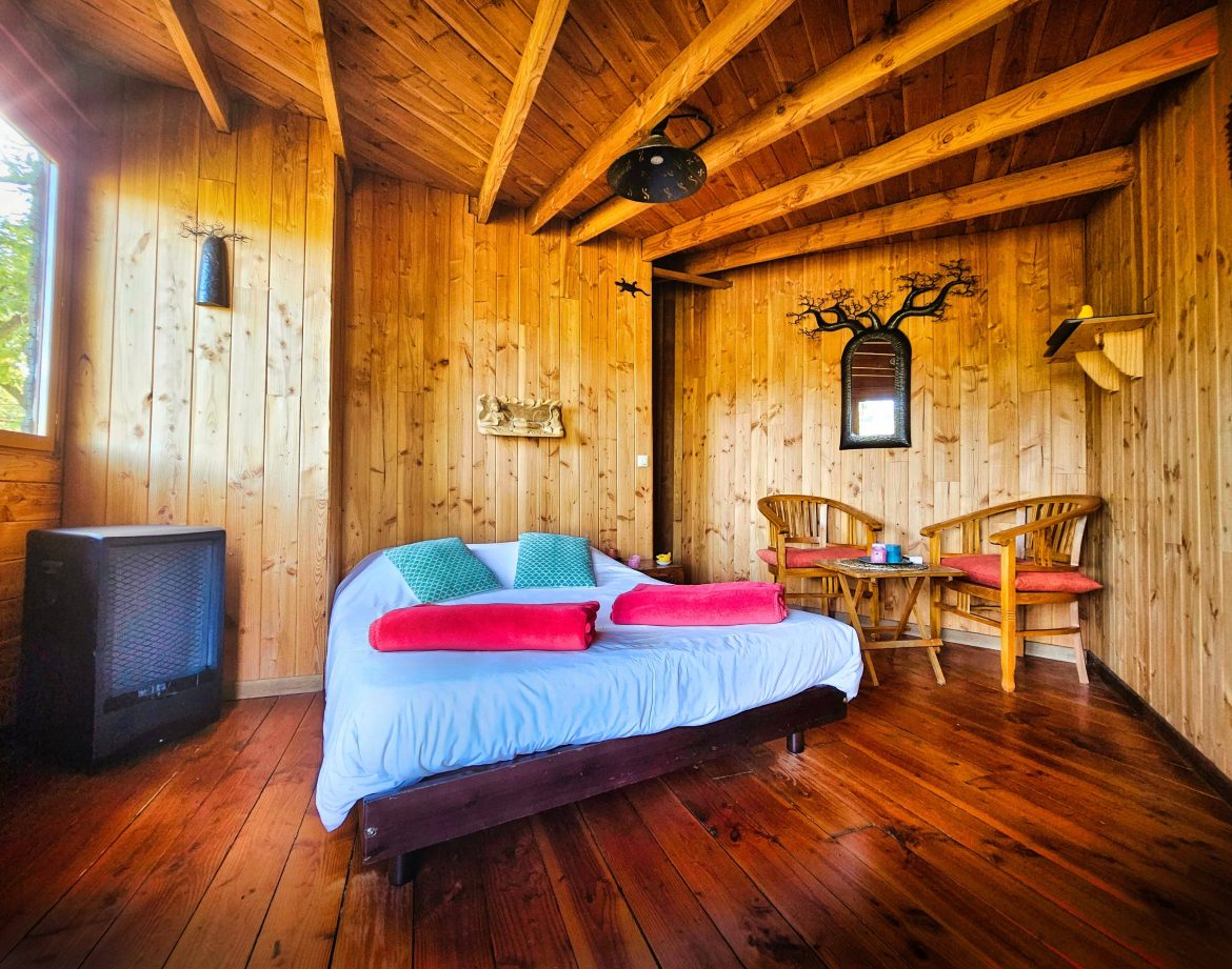 Cabane en bois cosy à Limousin, avec un lit douillet et des chaises en rotin.