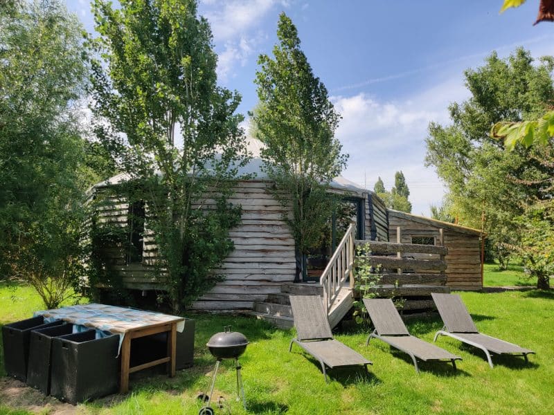 Yourte en bois à Basse-Normandie, entourée darbres et de chaises longues.
