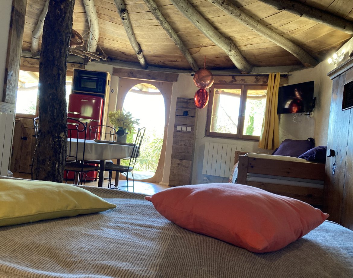 Hébergement insolite en cabane, intérieur chaleureux avec poutres en bois et coussins colorés.