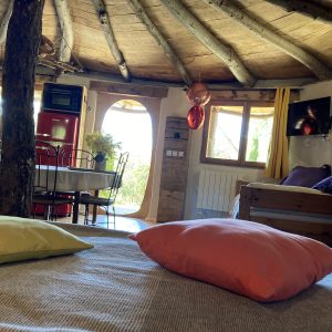 Hébergement insolite en cabane, intérieur chaleureux avec poutres en bois et coussins colorés.