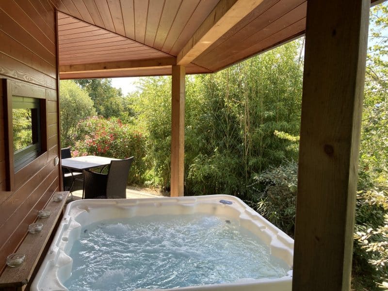 Chalet avec jacuzzi extérieur, entouré de verdure et dun espace détente.