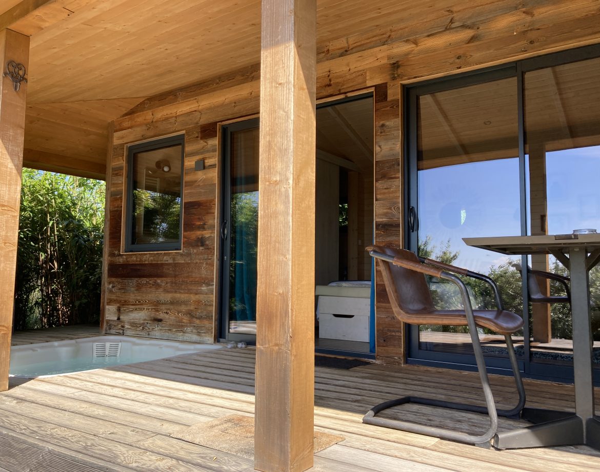 Cabane en bois avec terrasse et jacuzzi, entourée de verdure à Languedoc-Roussillon.