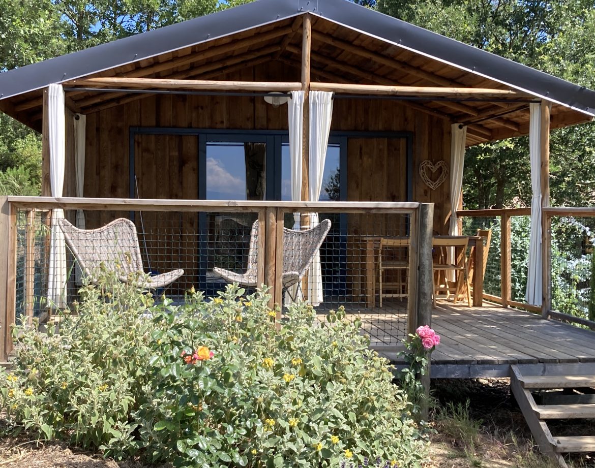 Cabane en bois avec terrasse, entourée de verdure et fleurs colorées.