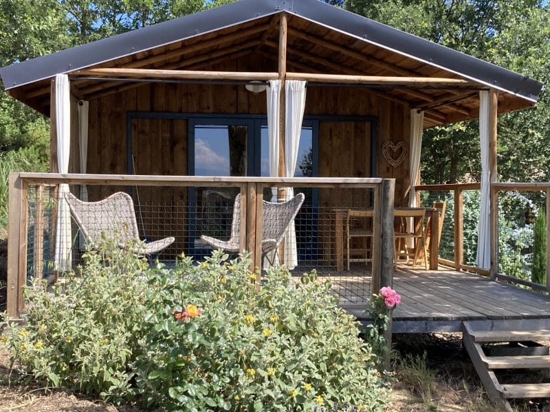 Cabane en bois avec terrasse, entourée de verdure et fleurs colorées.