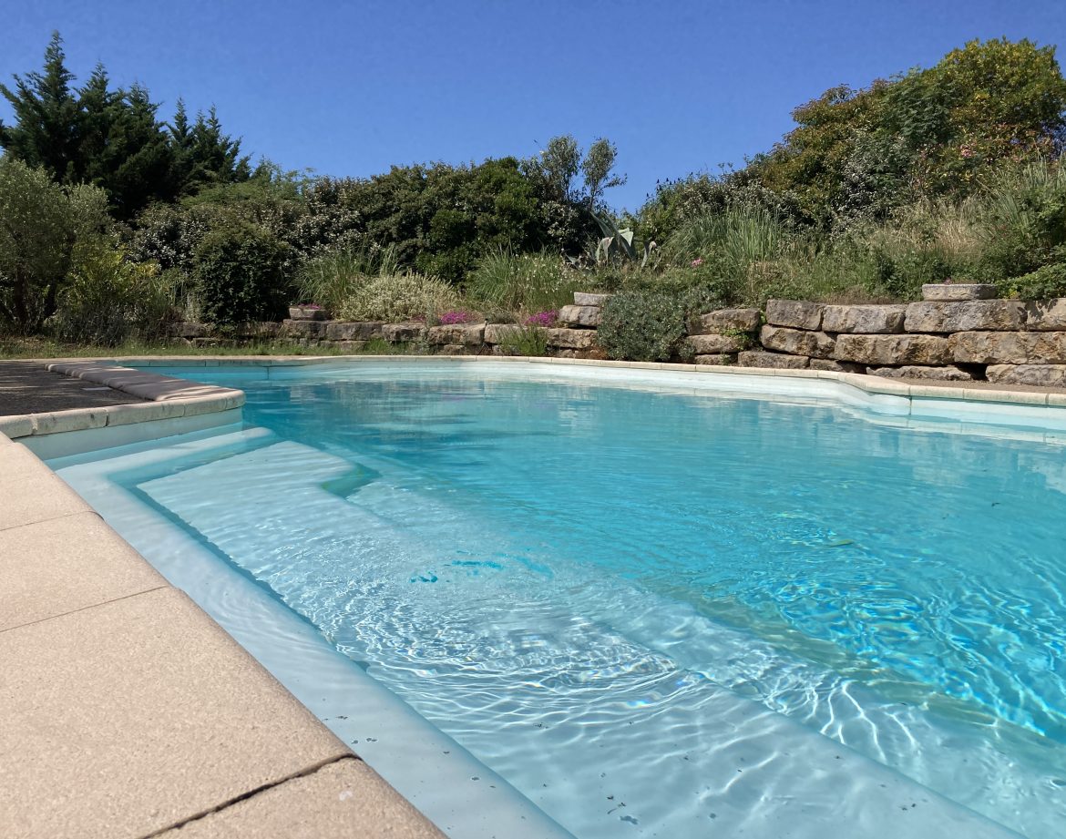 Hébergement insolite en Languedoc-Roussillon avec piscine turquoise entourée de verdure.