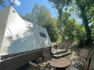 Tipi en Basse-Normandie, entouré de verdure, avec chaises en bois et table.