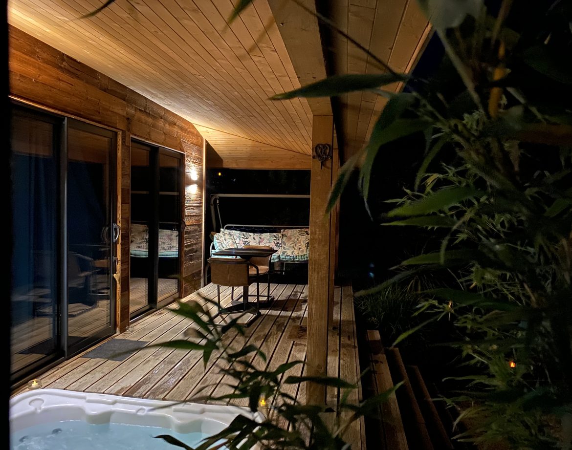 Cabane en bois avec terrasse, jacuzzi et ambiance nocturne relaxante.