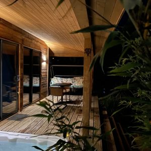 Cabane en bois avec terrasse, jacuzzi et ambiance nocturne relaxante.