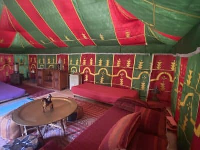 Tente berbère colorée avec coussins rouges et verts, ambiance chaleureuse et accueillante.