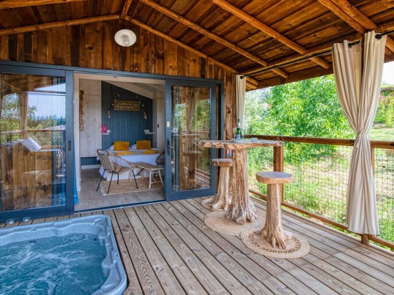 Chalet en bois avec terrasse, jacuzzi et vue sur la nature verdoyante.