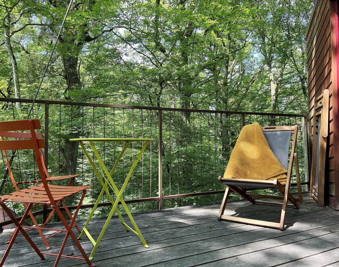 Cabane perchée en Bourgogne, avec balcon en bois et vue sur la forêt verdoyante.