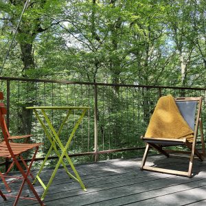 Cabane perchée en Bourgogne, avec balcon en bois et vue sur la forêt verdoyante.