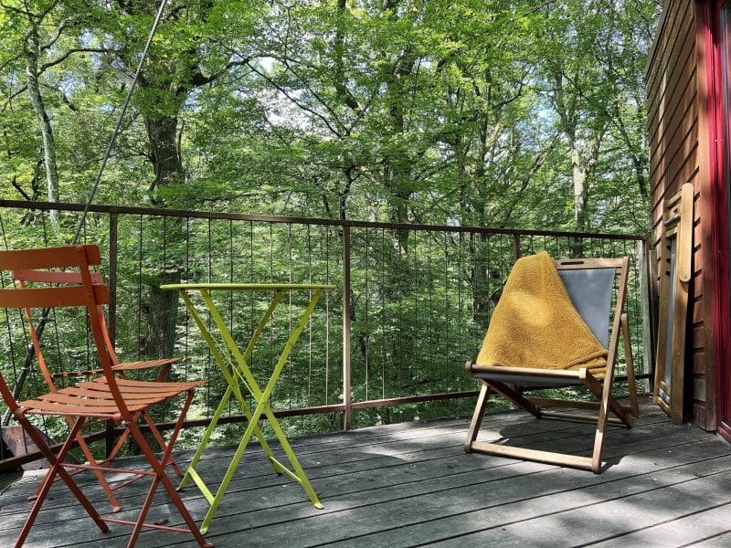 Chalet en bois avec balcon, chaises colorées et vue sur la forêt verdoyante.