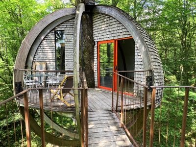 Cabane suspendue en bois, perchée dans les arbres avec vue sur la forêt verdoyante.